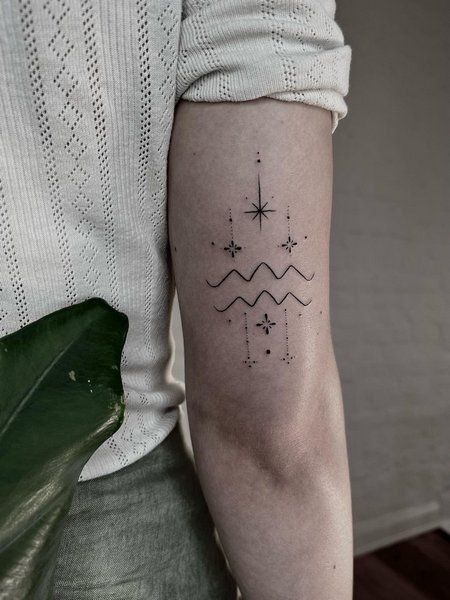 Minimalist geometric tattoo on arm with stars, lines, and wave patterns. Modern black ink design on a person's upper arm.