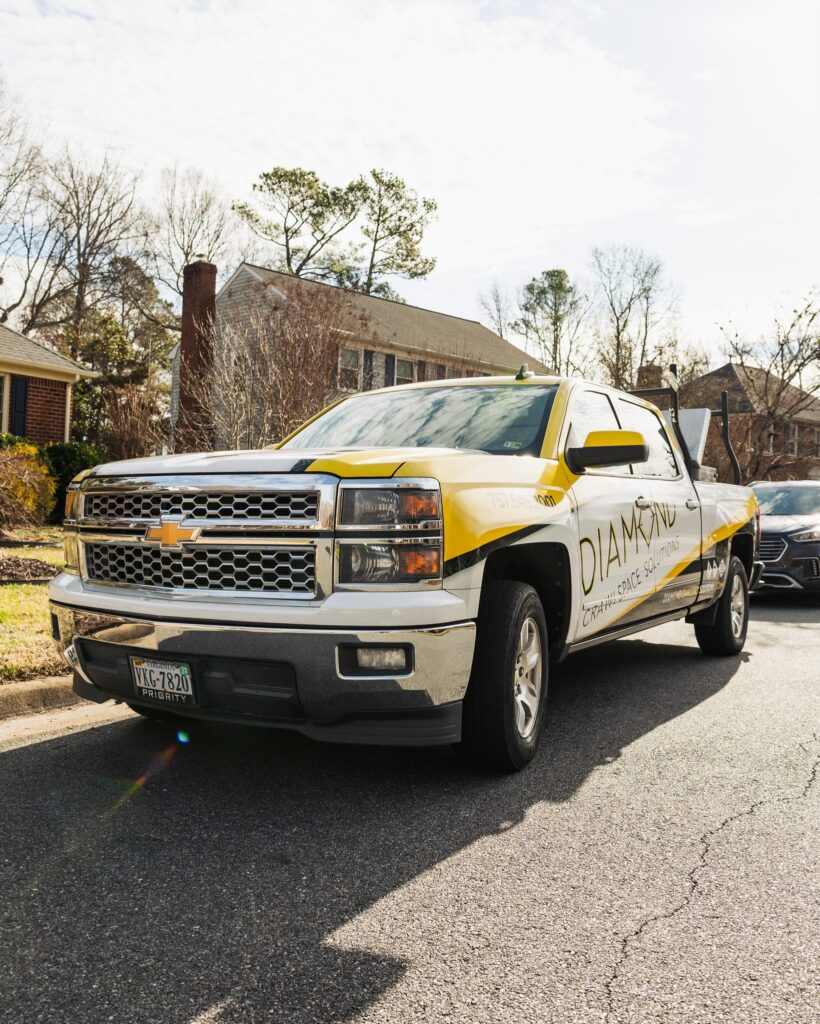 Yellow and white Chevrolet truck parked on a residential street, featuring Diamond Crawl Space Solutions branding on the side.