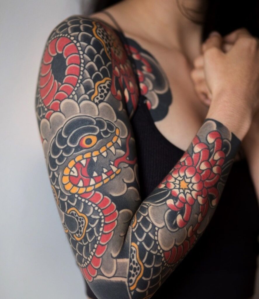 Intricate Japanese-style snake and flower sleeve tattoo on a person's arm, featuring bold red, black, and yellow colors.