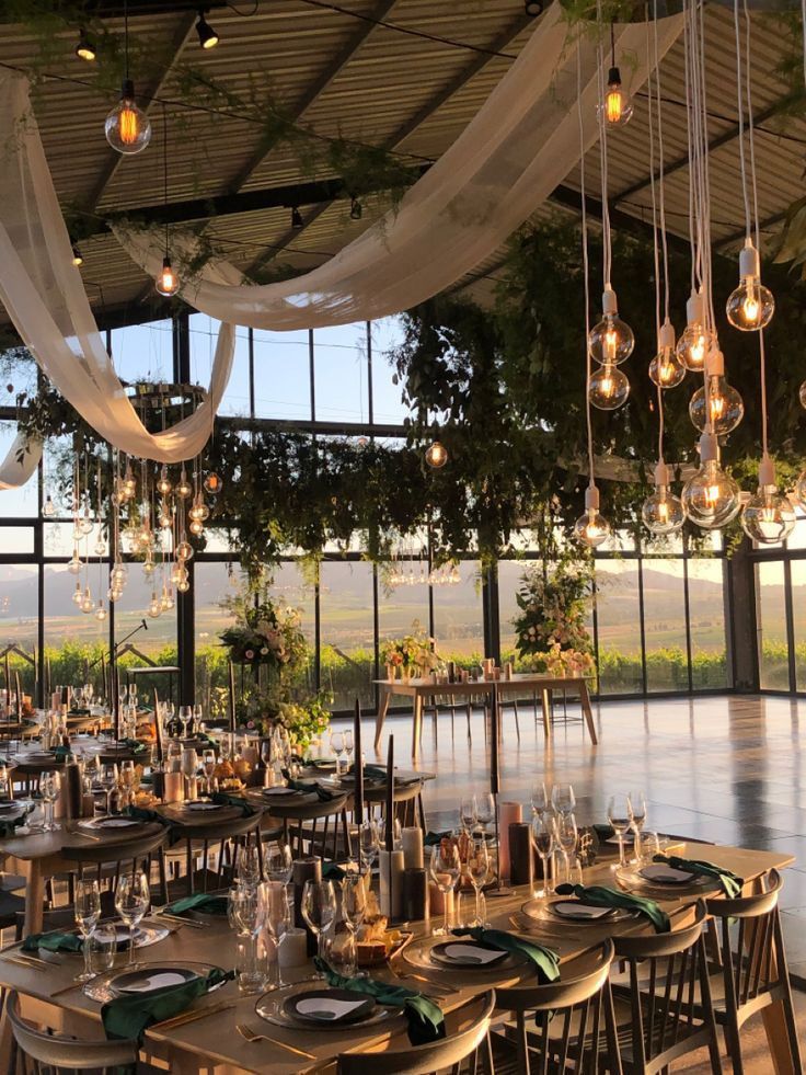 _ 5 Elegant wedding venue with rustic decor, hanging lights, and outdoor views. Tables set with green accents and floral arrangements. | Sky Rye Design Elegant wedding venue with rustic decor, hanging lights, and outdoor views. Tables set with green accents and floral arrangements.