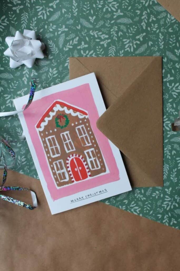 Festive Christmas card with gingerbread house design on green background, placed by brown envelope and bow.