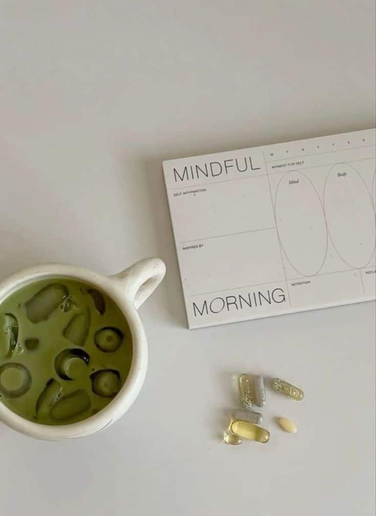 _ 5 Cup of iced matcha, supplements, and a Mindful Morning planner on a white table for a healthy start to the day. | Sky Rye Design Cup of iced matcha, supplements, and a Mindful Morning planner on a white table for a healthy start to the day.
