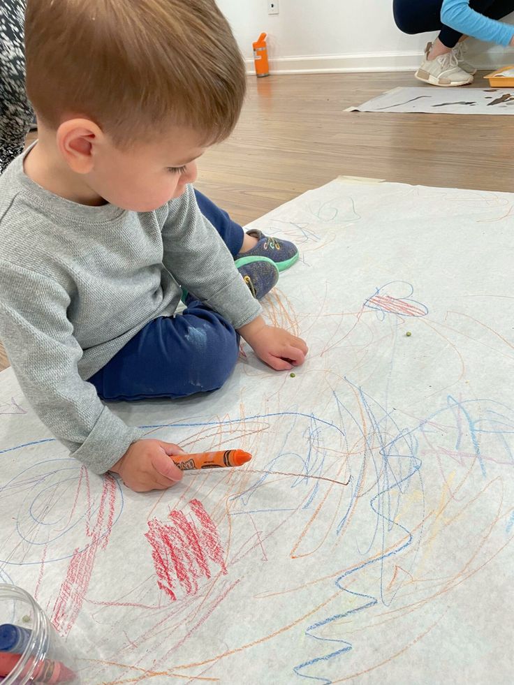 Toddler drawing with crayons on large paper, engaged in creative playtime.