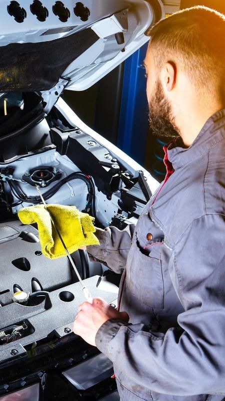 5 motores de carro que duram muito e passam longe da oficina Mechanic checking engine oil with dipstick under car hood in workshop. | Sky Rye Design Mechanic checking engine oil with dipstick under car hood in workshop.