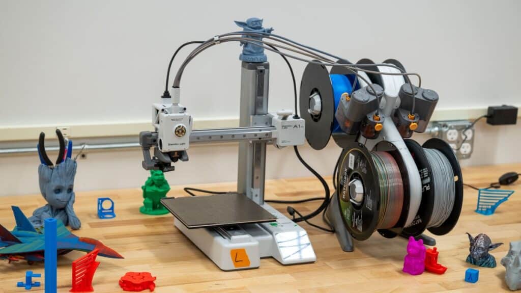 3D printer on a workbench with colorful filament spools and printed models.