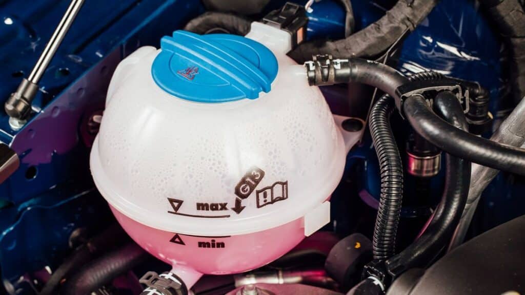 52b818fc4e673e00c354b65d2626e7f5 Close-up of a car coolant reservoir with a blue cap, showing maximum and minimum fill markings within an engine compartment. | Sky Rye Design Close-up of a car coolant reservoir with a blue cap, showing maximum and minimum fill markings within an engine compartment.