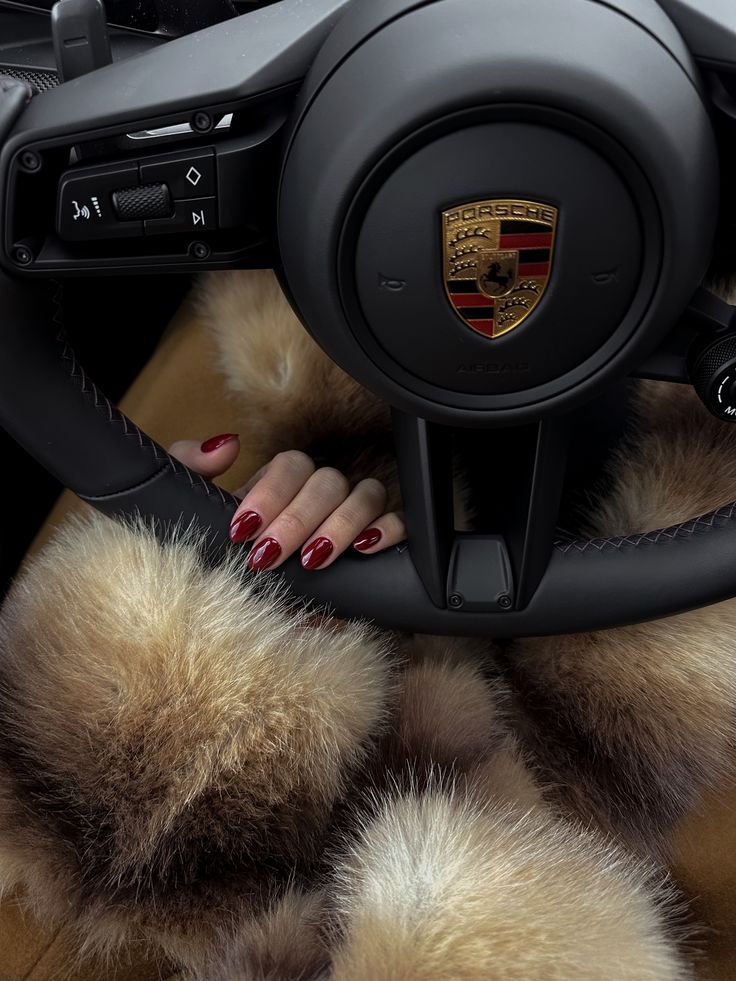 Luxurious steering of a Porsche with red manicured nails and a fur jacket captured in rich detail, symbolizing elegance and style.