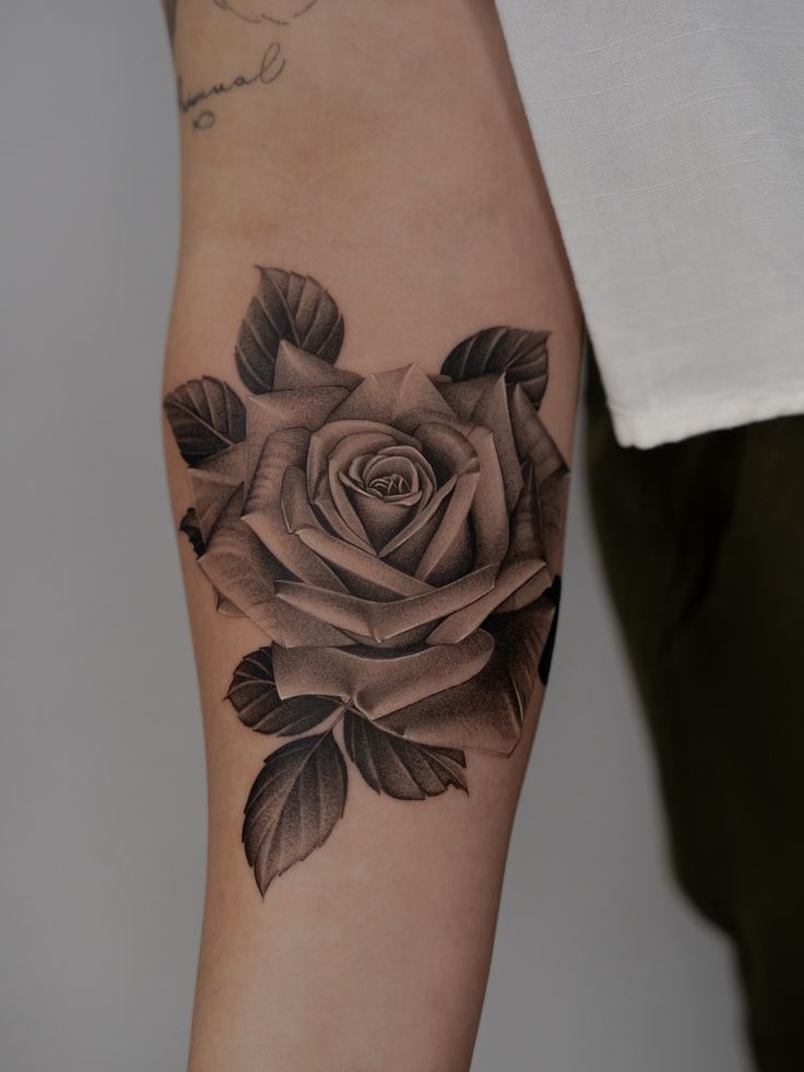Black and gray rose tattoo on forearm, detailed shading and intricate petal design, showcasing professional artistry.