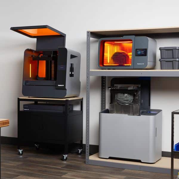 Modern 3D printers in a workspace, featuring open and enclosed designs with illuminated interiors for professional use and innovation.
