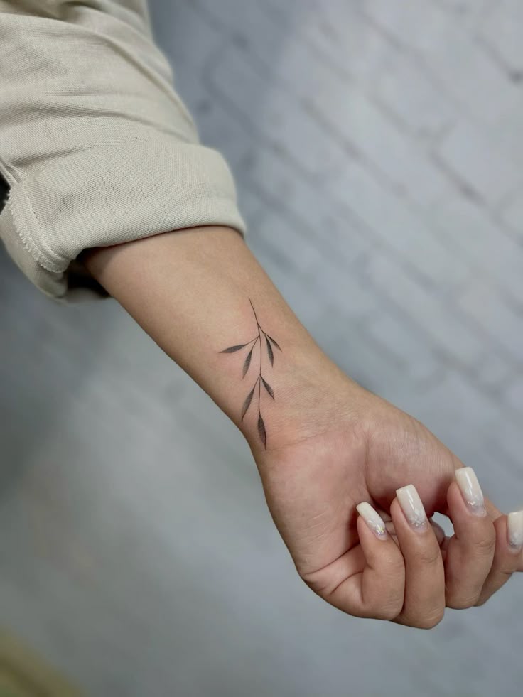 56f7afae6903d25080bcc3fccbc6d8d4 Minimalist branch tattoo on a person's forearm with white manicured nails, against a light background. | Sky Rye Design Minimalist branch tattoo on a person's forearm with white manicured nails, against a light background.