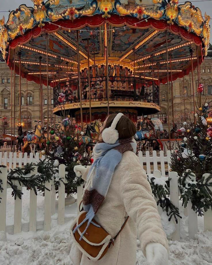 Woman in winter clothes enjoying a colorful, illuminated carousel at a festive carnival in snowy surroundings.