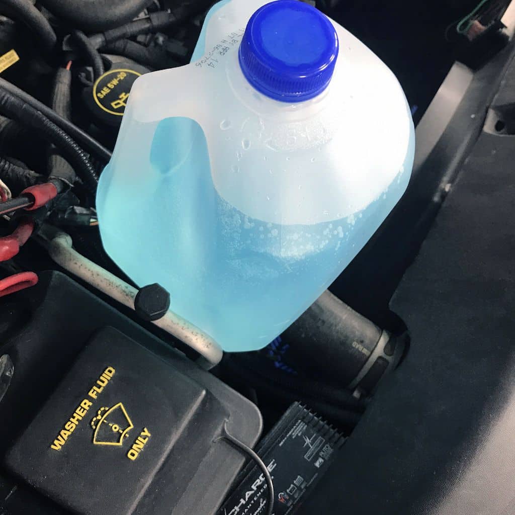 5bccba976672450d48a82233b3ec2ca7 Blue windshield washer fluid in a plastic jug being filled in a car's washer reservoir under the hood for maintenance. | Sky Rye Design Blue windshield washer fluid in a plastic jug being filled in a car's washer reservoir under the hood for maintenance.