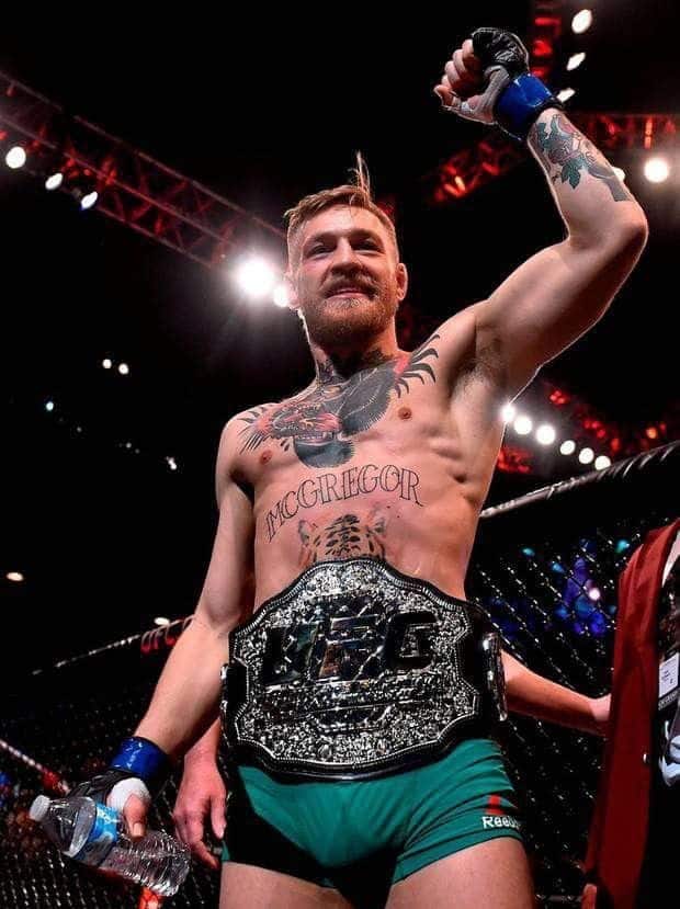 5cf4251ab5810a186ceb3da37ba5a56a MMA fighter celebrates victory, holding UFC championship belt in the octagon, wearing green shorts and showing tattoos, cheering crowd. | Sky Rye Design MMA fighter celebrates victory, holding UFC championship belt in the octagon, wearing green shorts and showing tattoos, cheering crowd.