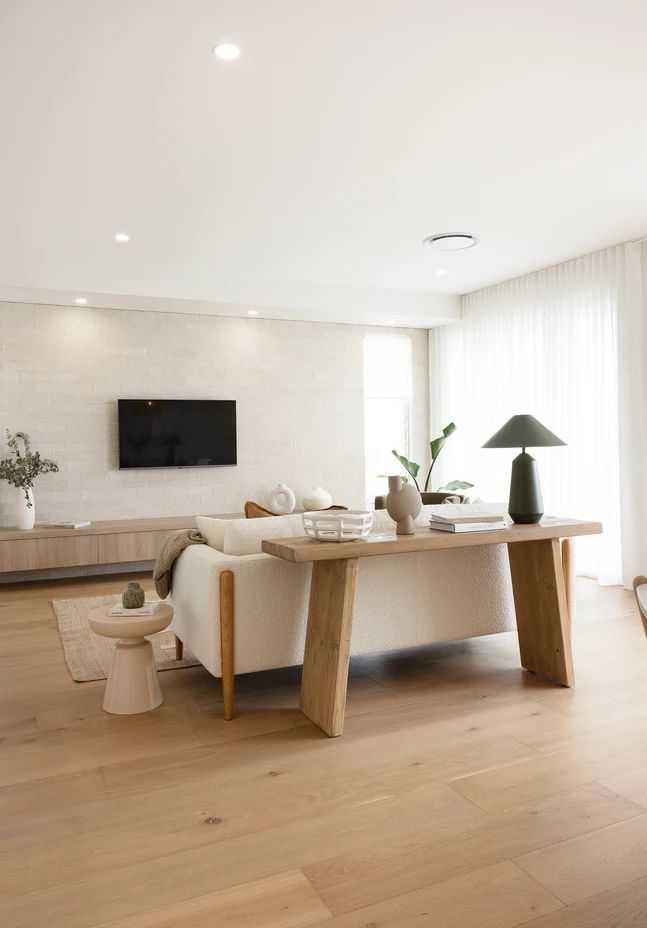 Modern living room with wooden floors, cozy sofa, decor accents, and natural lighting from large windows.