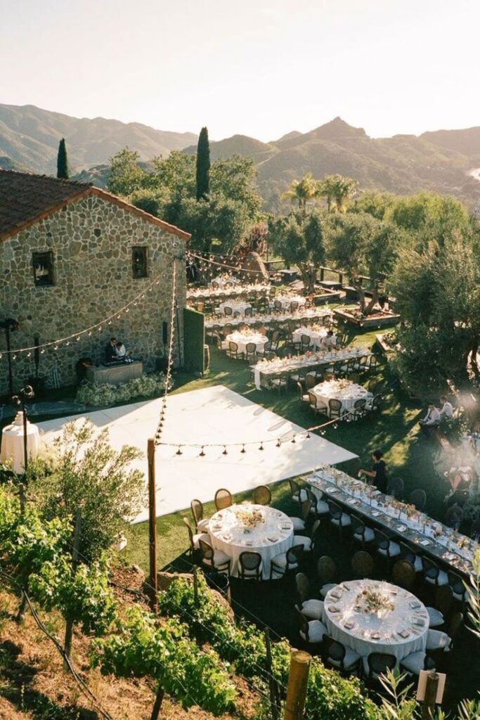 _ 6 Outdoor wedding venue with round tables, string lights, and mountain views at sunset, creating a romantic, rustic ambiance. | Sky Rye Design Outdoor wedding venue with round tables, string lights, and mountain views at sunset, creating a romantic, rustic ambiance.