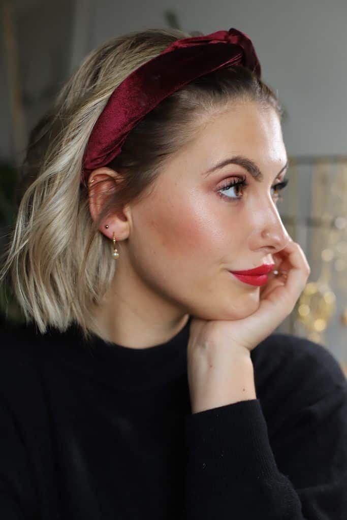 _ 6 Woman with a red headband and short blonde hair gazes thoughtfully, hand resting on chin. | Sky Rye Design Woman with a red headband and short blonde hair gazes thoughtfully, hand resting on chin.