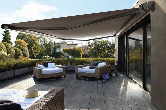 Modern patio with wicker sofas under a large retractable awning, overlooking a lush garden. Ideal outdoor living space for relaxation.
