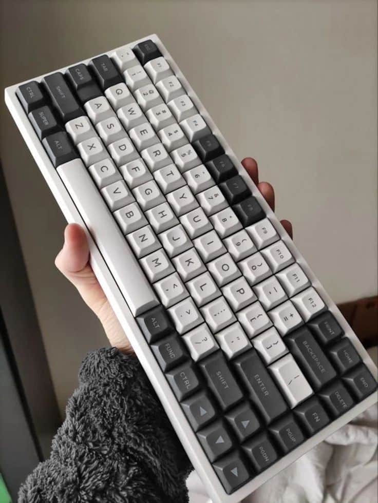Person holding a mechanical keyboard with a sleek, minimalist design featuring black and white keys. Ideal for gaming and typing enthusiasts.