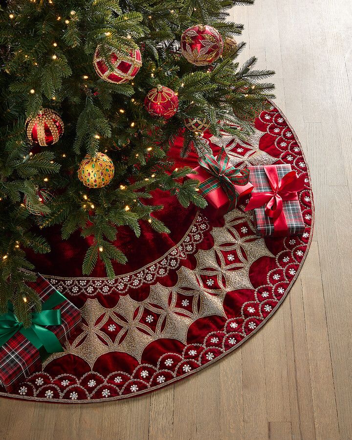 Christmas tree with red and gold ornaments, gifts, and an elegant red tree skirt on a wooden floor.