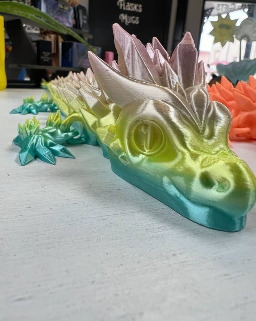 Colorful 3D-printed dragon figurine with intricate details on a table. Perfect for fantasy-themed decor or collectible displays.