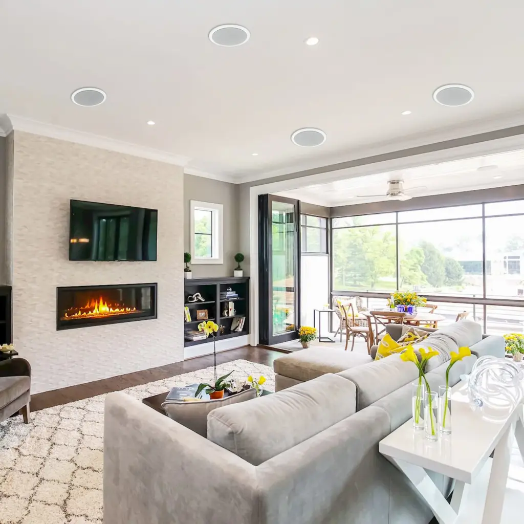 Modern living room with gray sectional sofa, wall-mounted TV, fireplace, and open views of a lush garden through sliding doors.