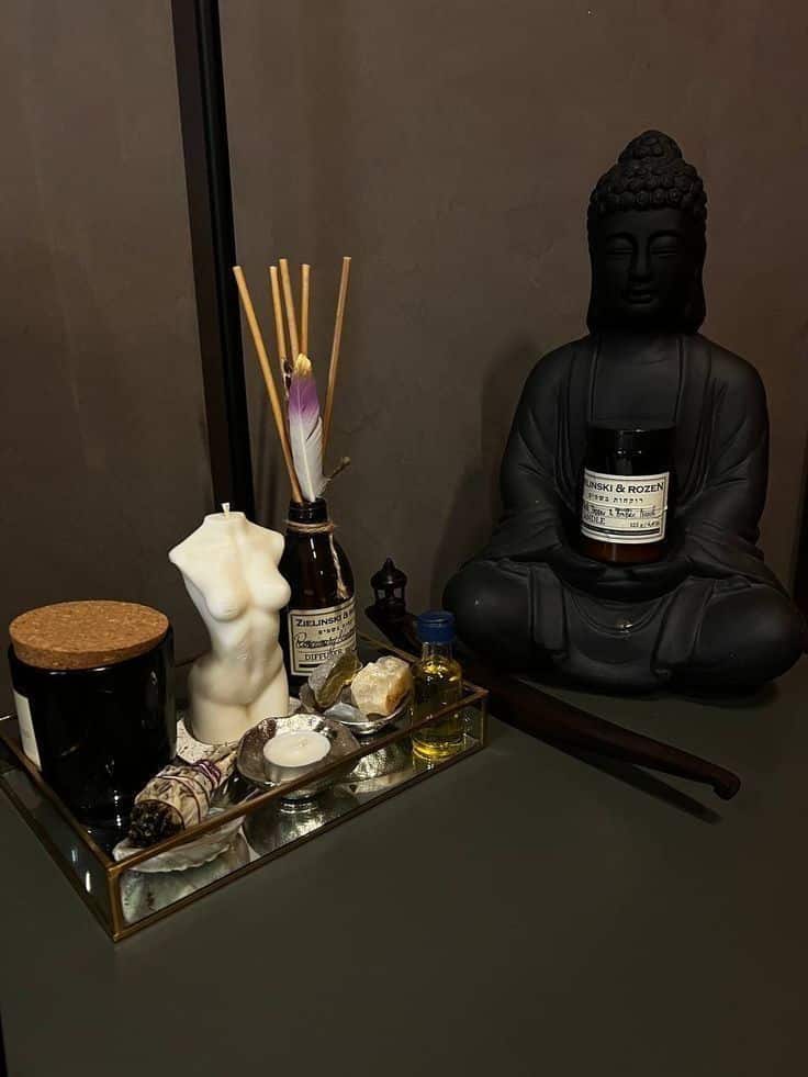 Zen-inspired decor with Buddha statue, candles, essential oils, and incense on a glass tray for a calming ambiance.
