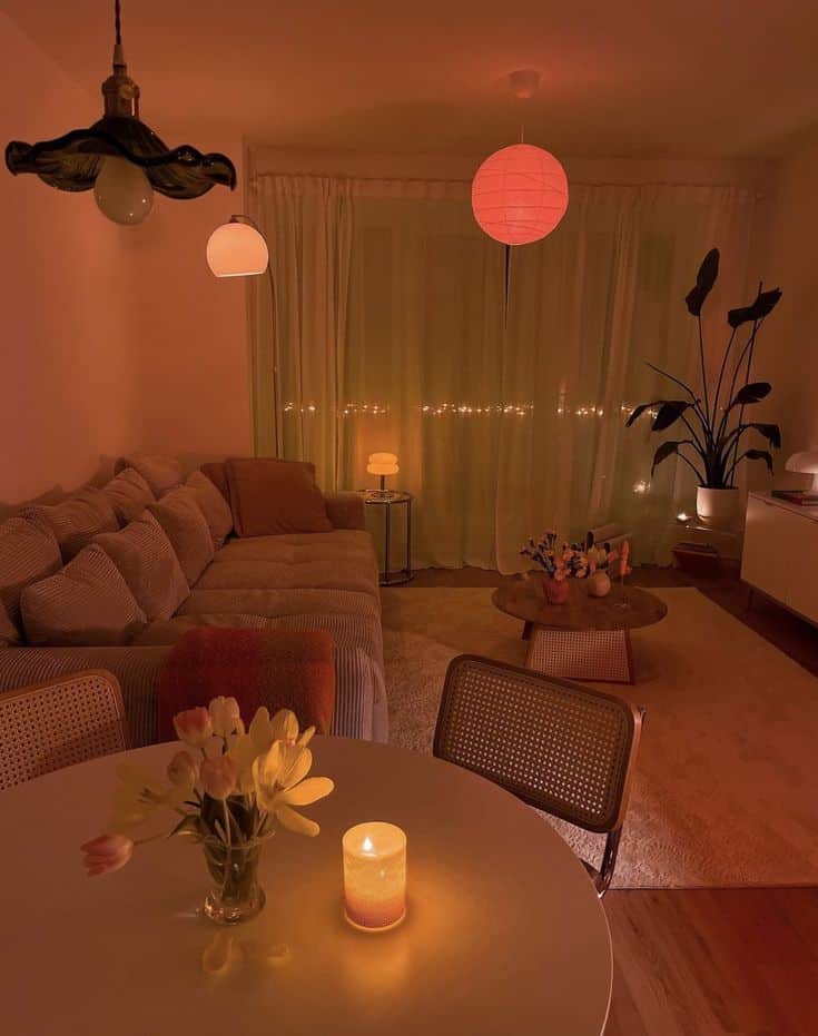 Cozy living room with warm lighting, soft beige sofa, plants, and candles on a round table, creating a relaxing evening ambiance.
