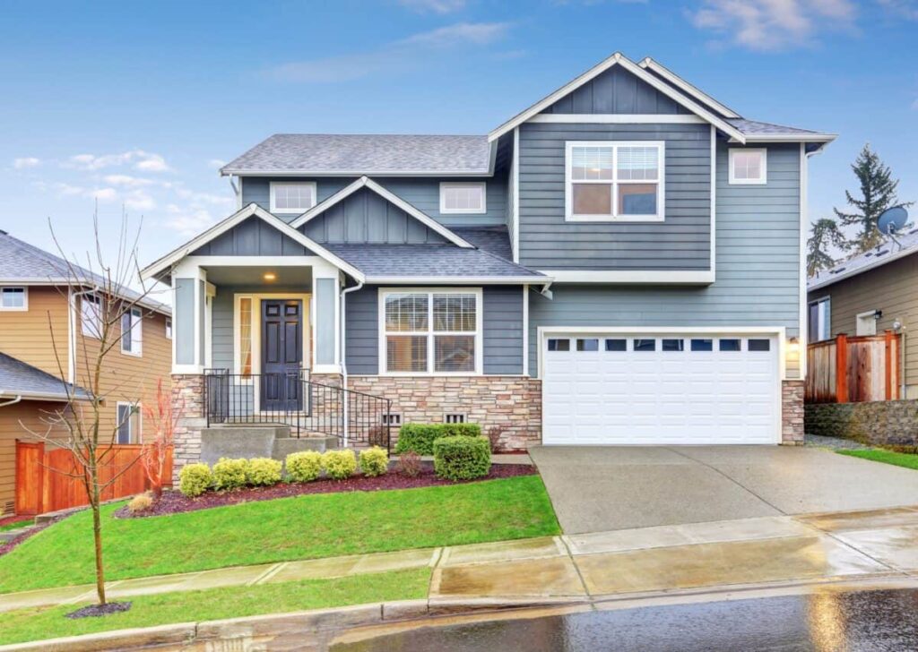 Modern gray two-story house with white garage, neat lawn, and stone accents under a blue sky.