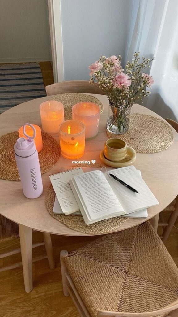 Cozy morning setup with candles, flowers, a notebook, and a cup on a wooden table, perfect for relaxation and inspiration.