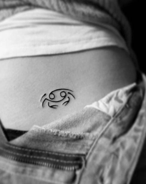 Small Cancer zodiac tattoo in black ink on the lower back, symbolizing the astrological sign.