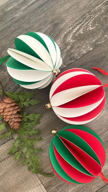 Festive paper ornaments in red, green, and white on a rustic wooden background with pine cone and greenery for Christmas decoration.