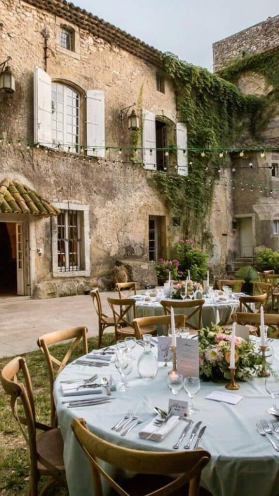 _ 7 Outdoor wedding reception setup with elegantly arranged tables and chairs, nestled against a rustic stone building draped in ivy. | Sky Rye Design Outdoor wedding reception setup with elegantly arranged tables and chairs, nestled against a rustic stone building draped in ivy.