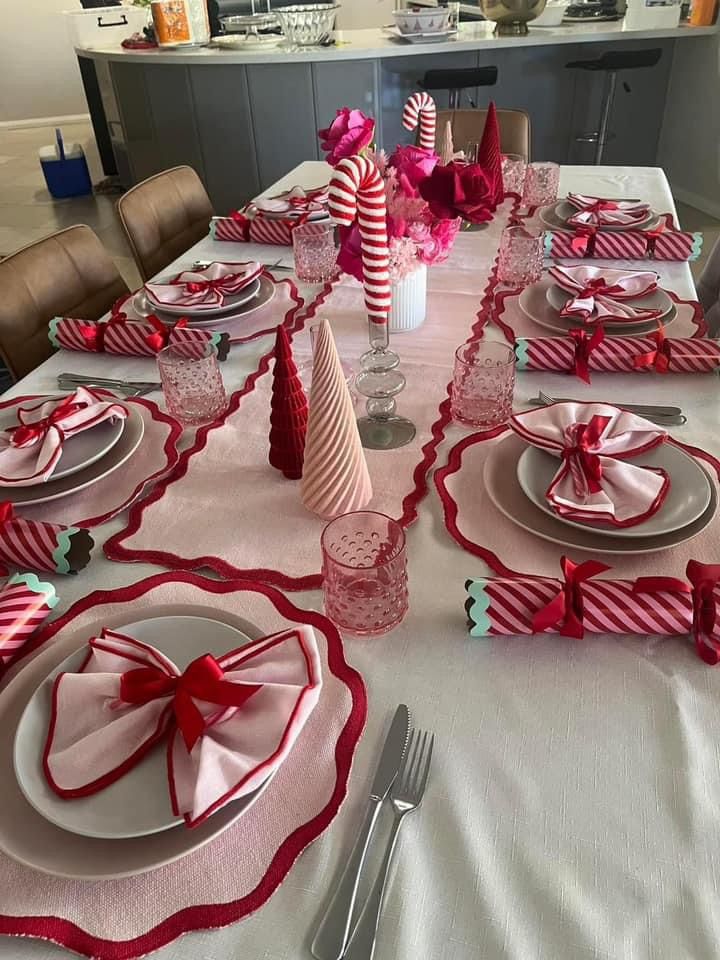 Festive dining table setting with pink and red decor, candy cane ornaments, and neatly arranged plates and napkins for a holiday celebration.