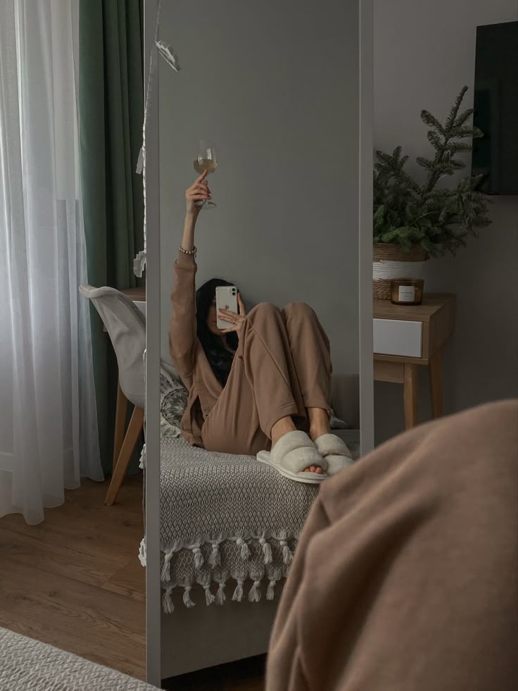 Cozy room setting with a person in loungewear holding a glass of wine, reflected in a mirror. Relaxed, comfortable home atmosphere.