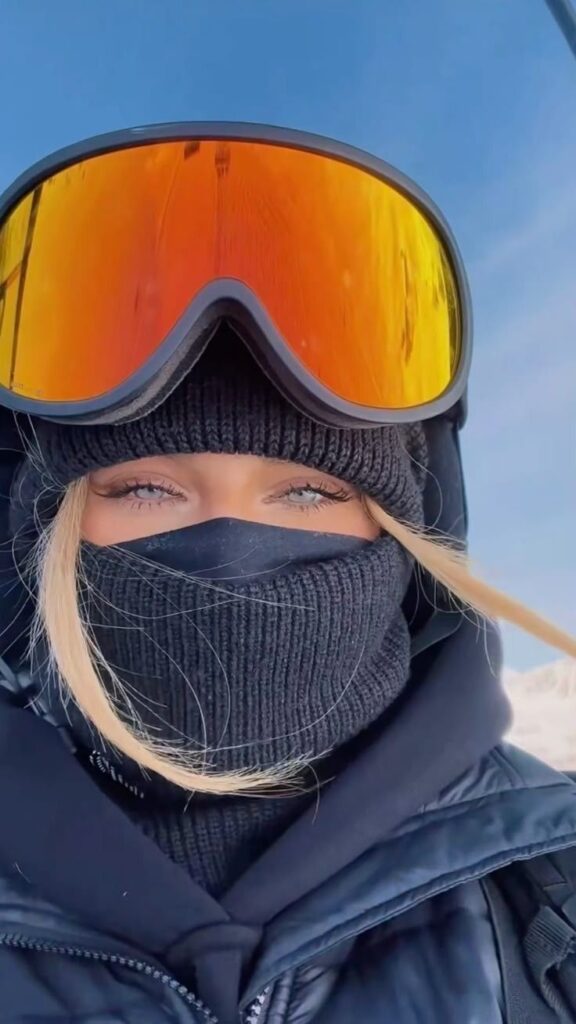 Person in winter gear with ski goggles, beanie, and face mask against a clear blue sky.