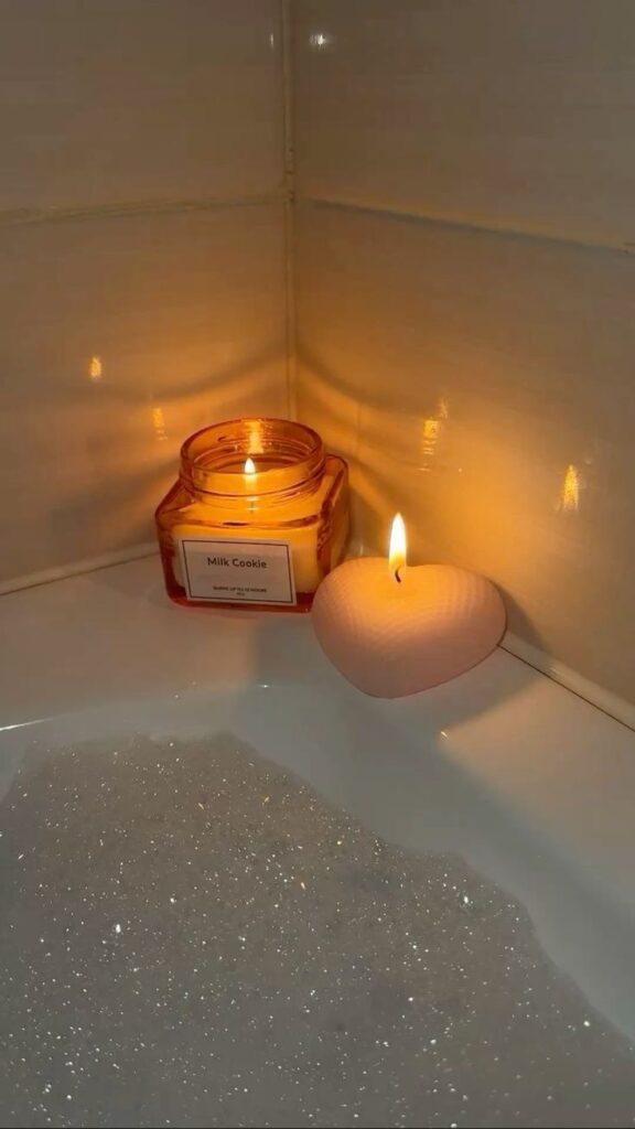 Cozy candlelit bath with milk cookie scented candle and heart-shaped candle, perfect for relaxing and unwinding in a bubble-filled tub.
