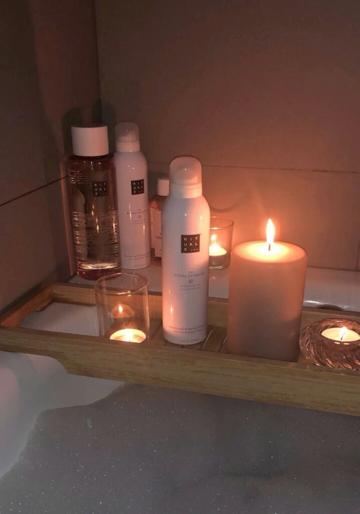 Candles and skincare bottles on a wooden tray create a relaxing spa-like ambiance in a bubble-filled bath.