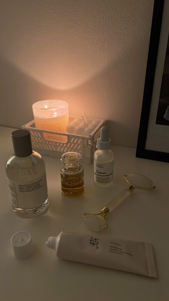 Skincare essentials and candle on a table, featuring serums, oils, cream, and a jade roller, creating a relaxing atmosphere.
