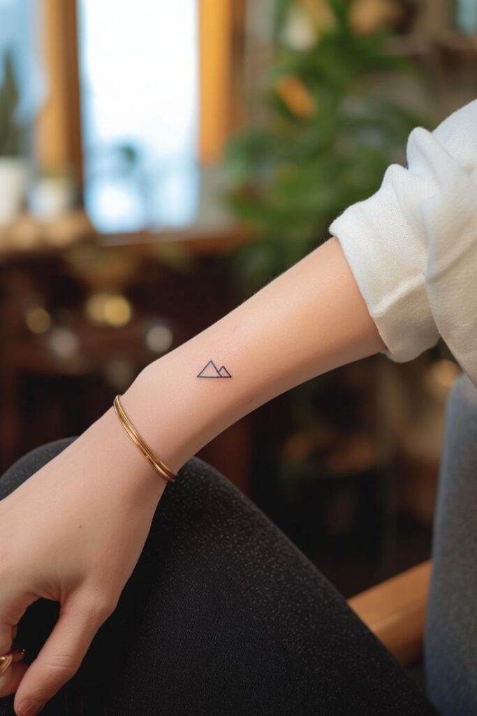 77 Chic and Simple Mountain Tattoo Design Ideas for Every Minimalist Minimalist triangle tattoo on forearm, person wearing a white sweater and bracelet, blurred indoor background. | Sky Rye Design Minimalist triangle tattoo on forearm, person wearing a white sweater and bracelet, blurred indoor background.