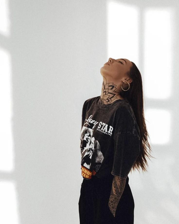 784c7c2bf21a6568af827c692b59720e Woman with tattooed neck and arms, wearing a graphic tee, gazes upward in a sunlit room. | Sky Rye Design Woman with tattooed neck and arms, wearing a graphic tee, gazes upward in a sunlit room.