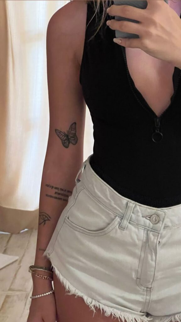 7afd2a8b-02fe-493c-b8aa-aa29aa2f13b0 Woman in black top and white shorts with tattoos, holding phone in mirror selfie. | Sky Rye Design Woman in black top and white shorts with tattoos, holding phone in mirror selfie.
