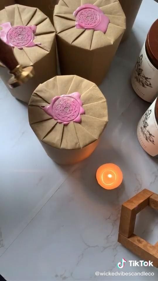 _ 8 Handcrafted candles with pink wax seals on a white surface, alongside a lit candle and decorative items. Elegant and cozy atmosphere. | Sky Rye Design Handcrafted candles with pink wax seals on a white surface, alongside a lit candle and decorative items. Elegant and cozy atmosphere.