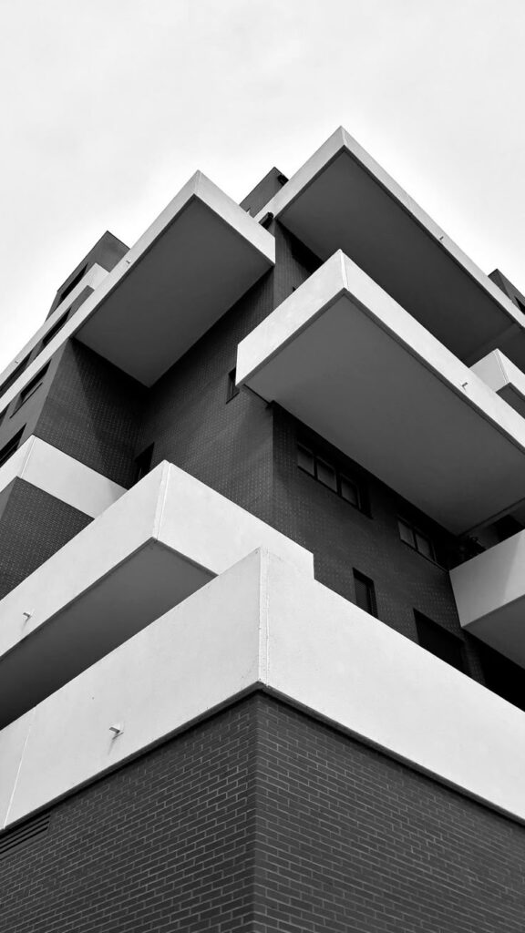 Modern architectural building in black and white, featuring geometric lines and extending balconies against a cloudy sky.