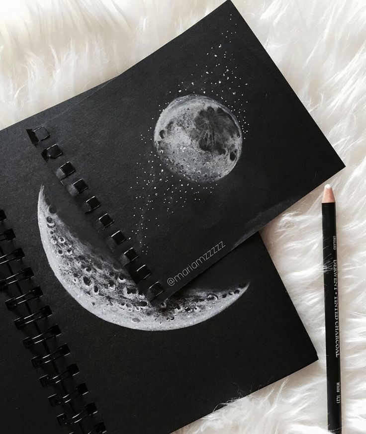 Charcoal moon sketches on black paper, featuring a crescent and full moon with stars, alongside a charcoal pencil, on a white surface.
