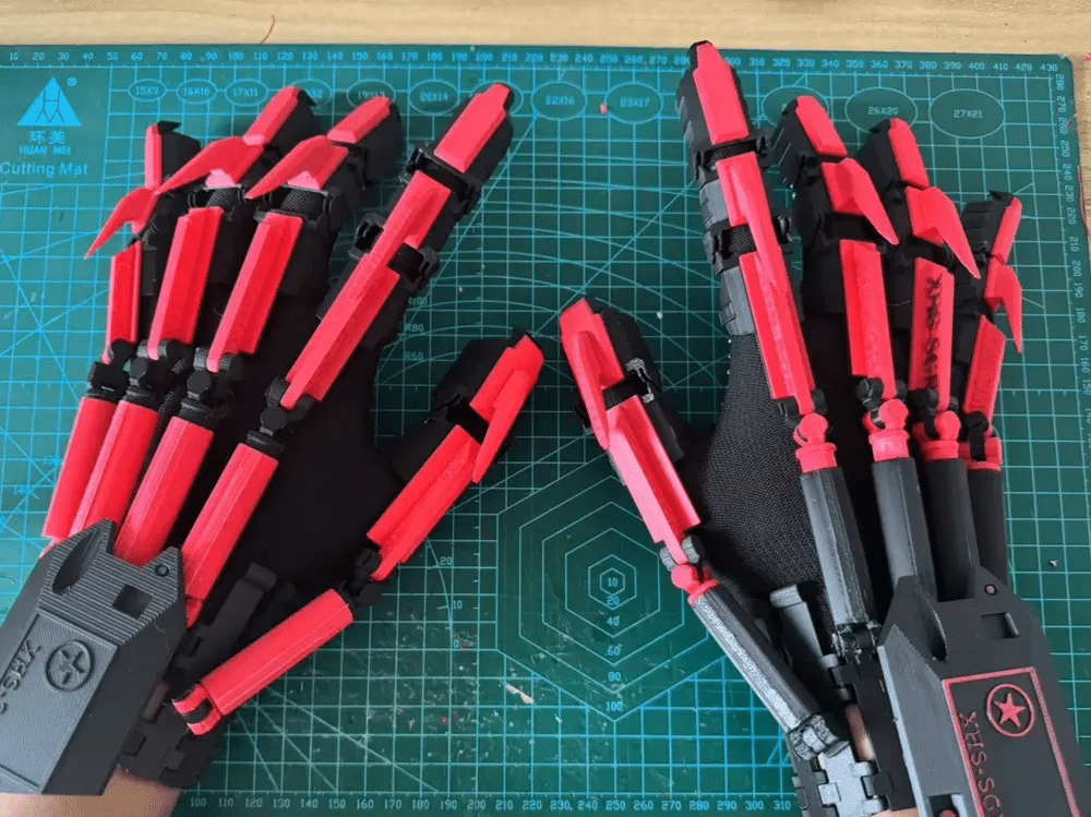 81a4a9e8-f380-44cb-aaac-4855280ada9d Red and black robotic gloves with intricate design on a cutting mat. | Sky Rye Design Red and black robotic gloves with intricate design on a cutting mat.