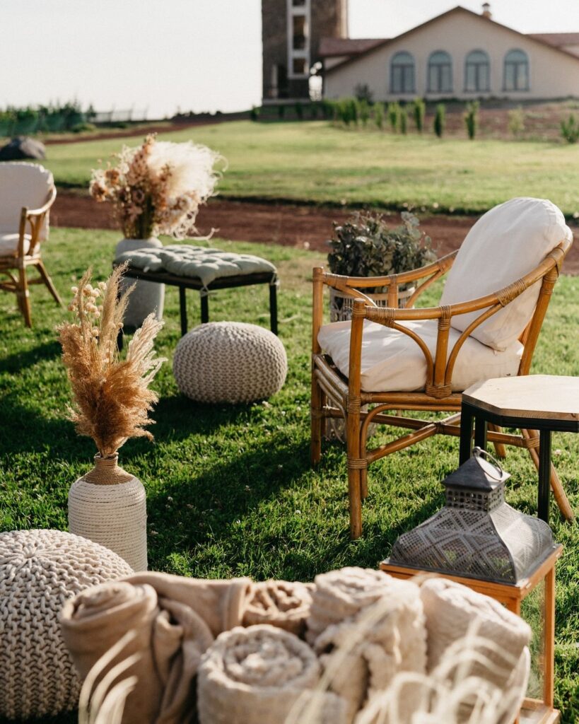 83988b69d038ff86ed36653491209599 Outdoor boho lounge setup with wicker chair, poufs, dried floral decor, and lantern on green lawn, ideal for rustic events or gatherings. | Sky Rye Design Outdoor boho lounge setup with wicker chair, poufs, dried floral decor, and lantern on green lawn, ideal for rustic events or gatherings.