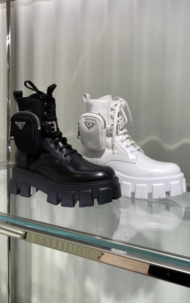 Black and white chunky boots with side pouches on a glass shelf, blending style with functionality in modern footwear design.