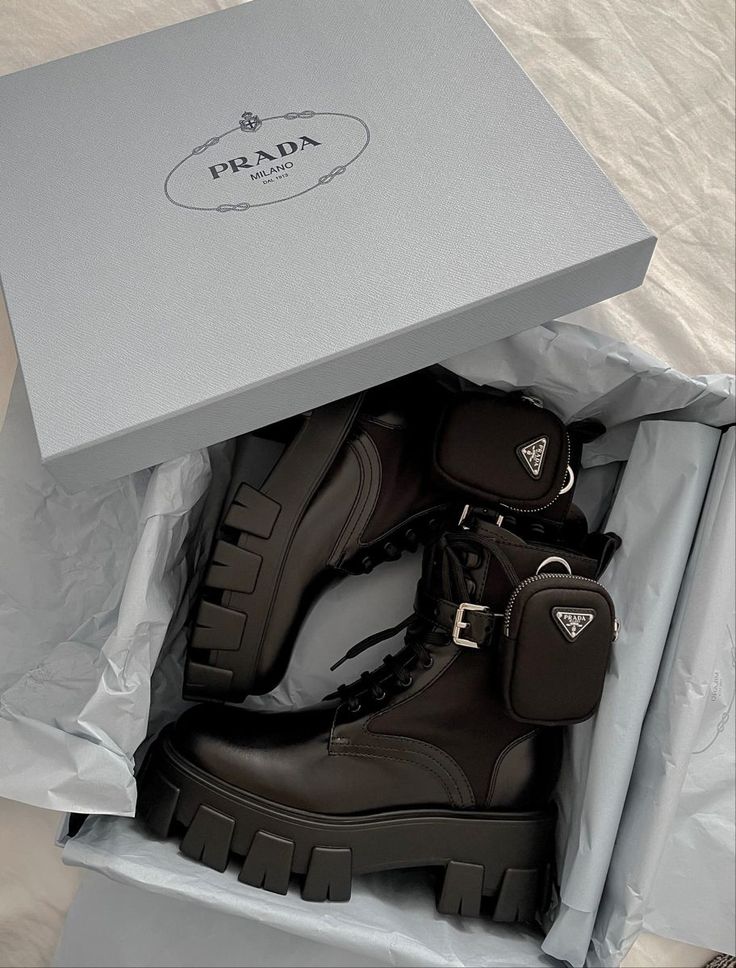 Prada combat boots in a designer box, featuring chunky soles and side pouches. Stylish, high-fashion footwear on display.