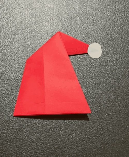 Origami Santa hat on a dark background, showcasing a festive holiday craft made from red paper with a white tip.