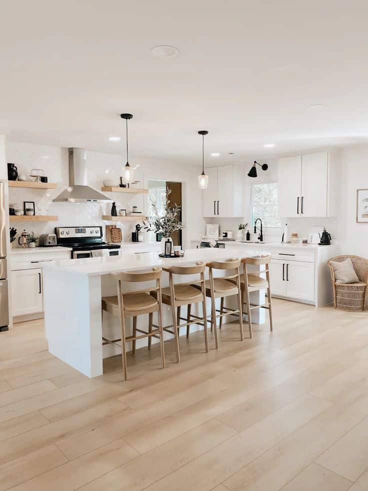 Modern white kitchen with island, wood stools, pendant lights, and open shelving. Bright, spacious, and stylish design.